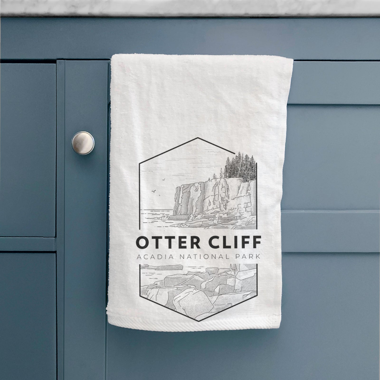 White hand towel printed with a black line art badge of Otter Cliff above the ocean, with the words Otter Cliff, Acadia National Park.
