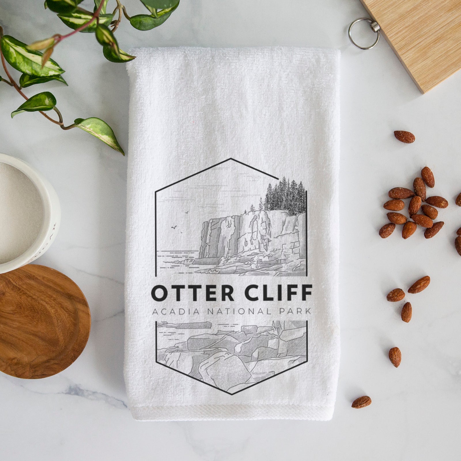 White hand towel printed with a black line art badge of Otter Cliff above the ocean, with the words Otter Cliff, Acadia National Park.