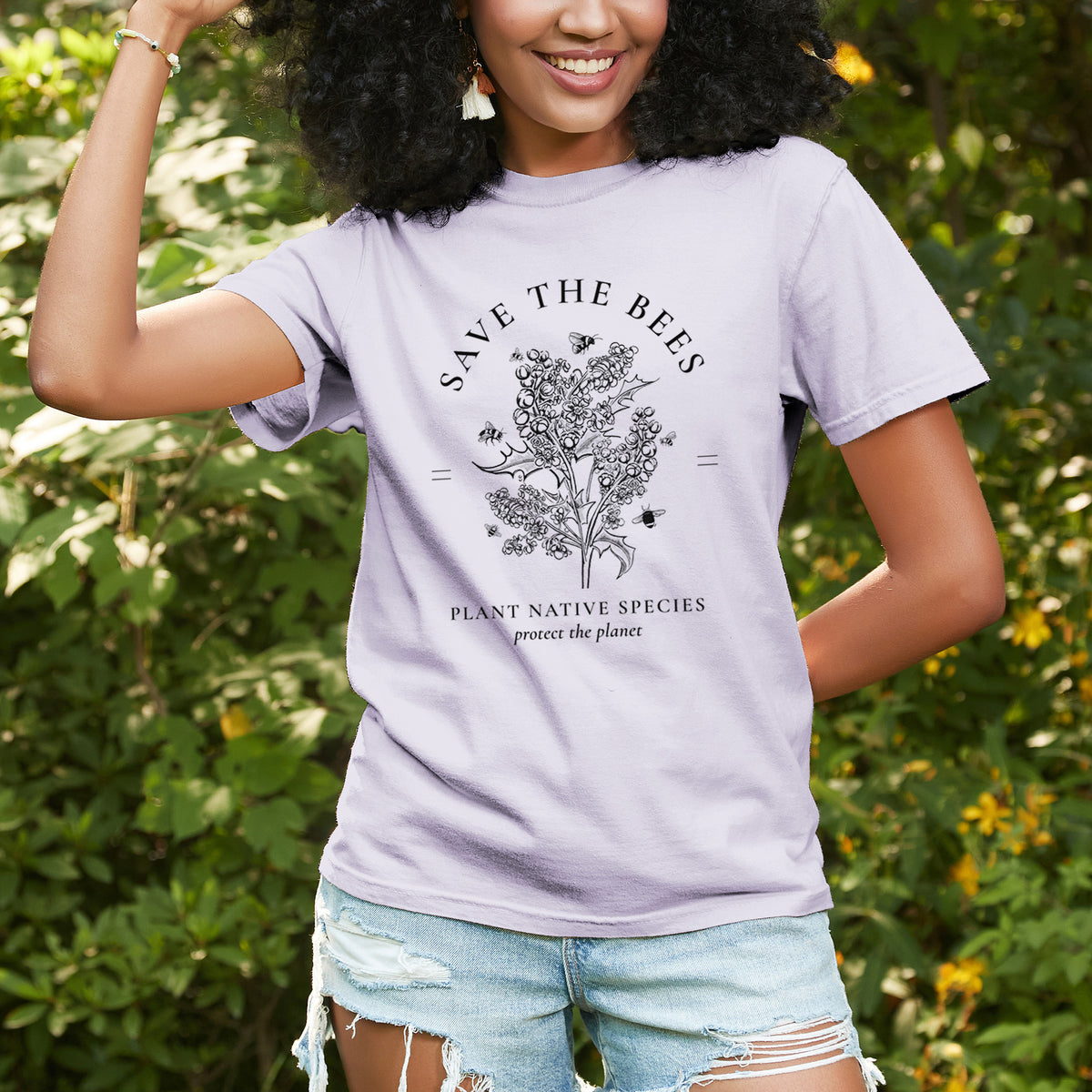 Woman wearing a Comfort Colors t-shirt printed with a black ink wildflower bouquet with bees, framed by the words Save the Bees, Plant Native Species, outdoors.