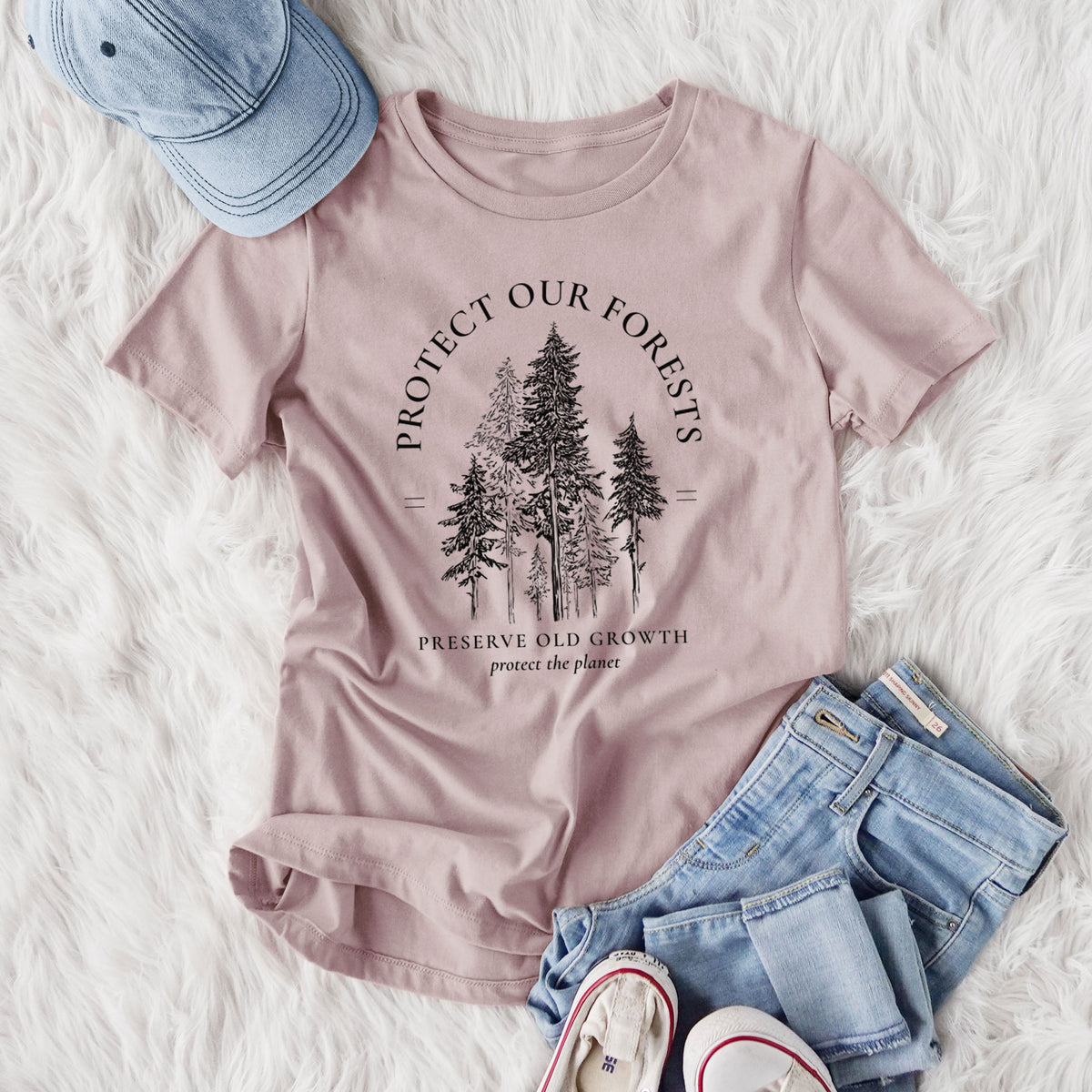 Women's relaxed fit cotton t-shirt printed with a black ink illustration of a stand of tall pine trees, framed by the words Protect Our Forests, Preserve Old Growth, styled flat on a white faux fur rug with jeans.