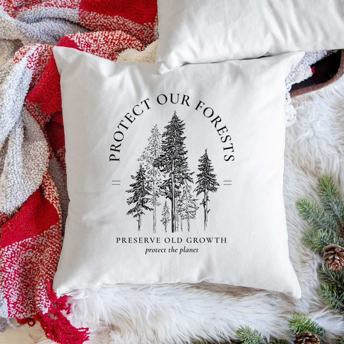White pillow cover printed with a black ink illustration of a stand of tall pine trees, framed by the words Protect Our Forests, Preserve Old Growth, on a woven chair.