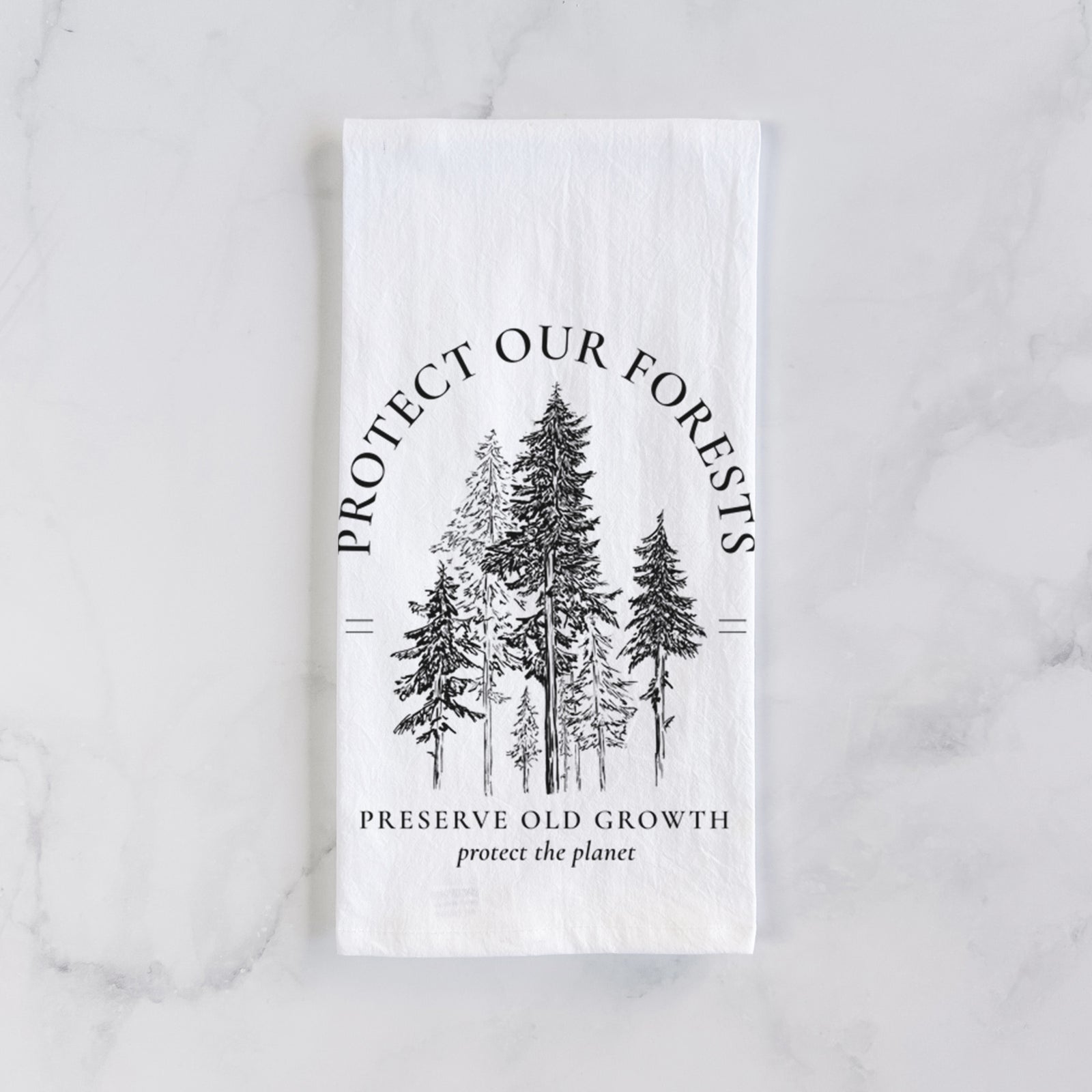 White cotton tea towel printed with a black ink illustration of a stand of tall pine trees, framed by the words Protect Our Forests, Preserve Old Growth, on a marble counter beside a round wooden cutting board and greenery.