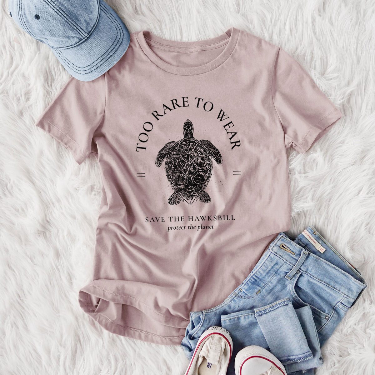 Women's relaxed fit cotton t-shirt printed with a black ink hawksbill sea turtle framed by the words Too Rare to Wear, Save the Hawksbill, styled flat on a white faux fur rug with jeans.