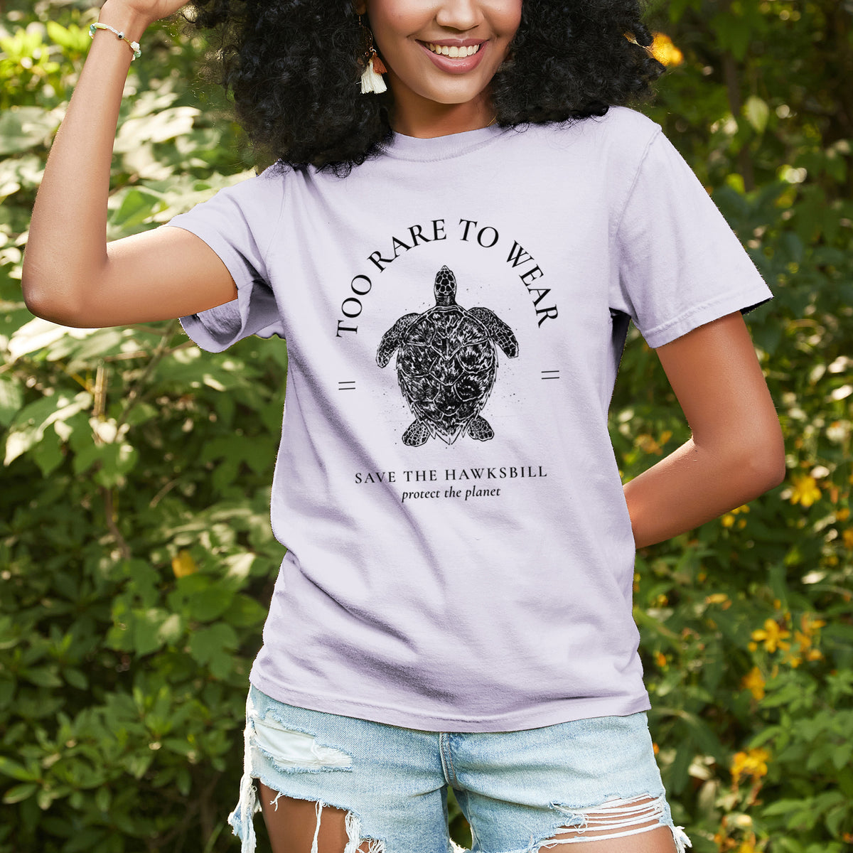 Woman wearing a Comfort Colors t-shirt printed with a black ink hawksbill sea turtle framed by the words Too Rare to Wear, Save the Hawksbill, outdoors.