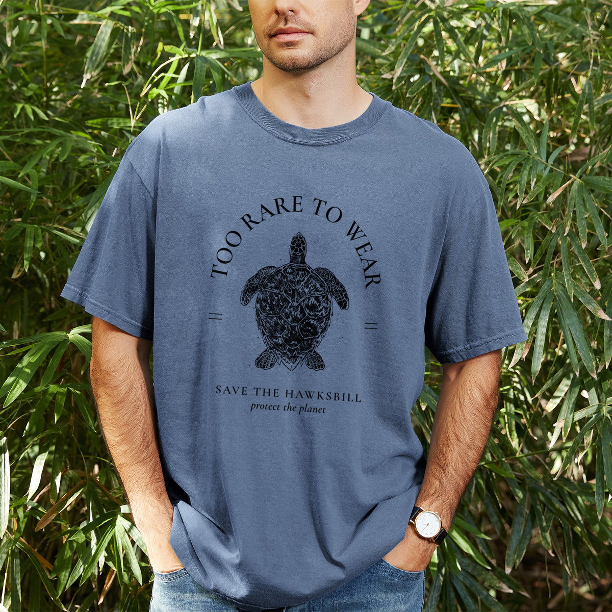 Man wearing a Comfort Colors t-shirt printed with a black ink hawksbill sea turtle framed by the words Too Rare to Wear, Save the Hawksbill, outdoors.