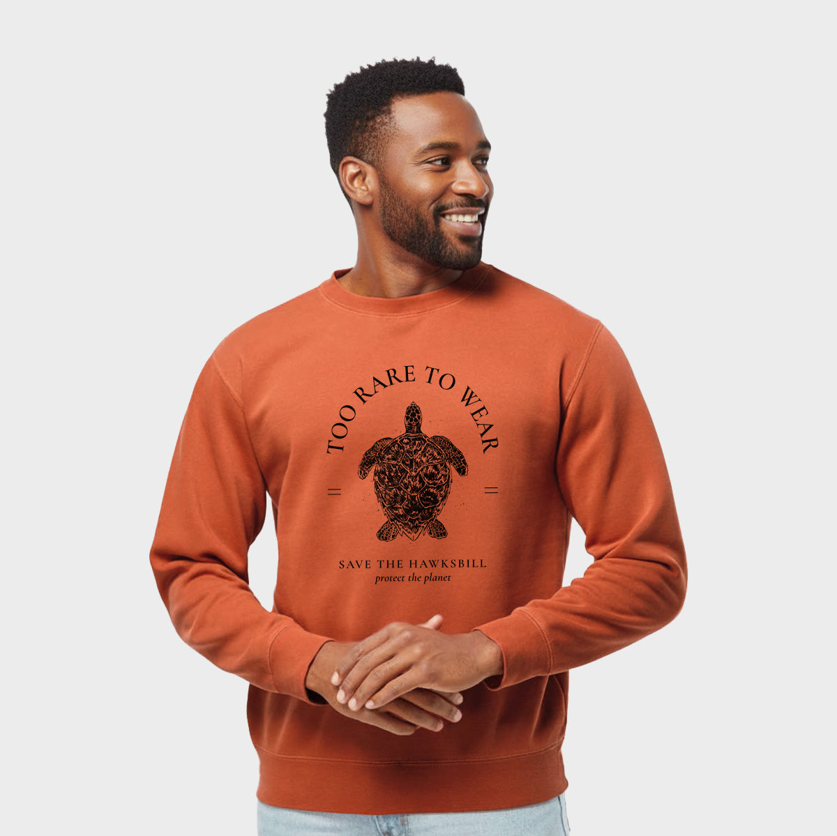 Model wearing an amber orange pigment dyed crewneck sweatshirt printed with a black ink hawksbill sea turtle framed by the words Too Rare to Wear, Save the Hawksbill.