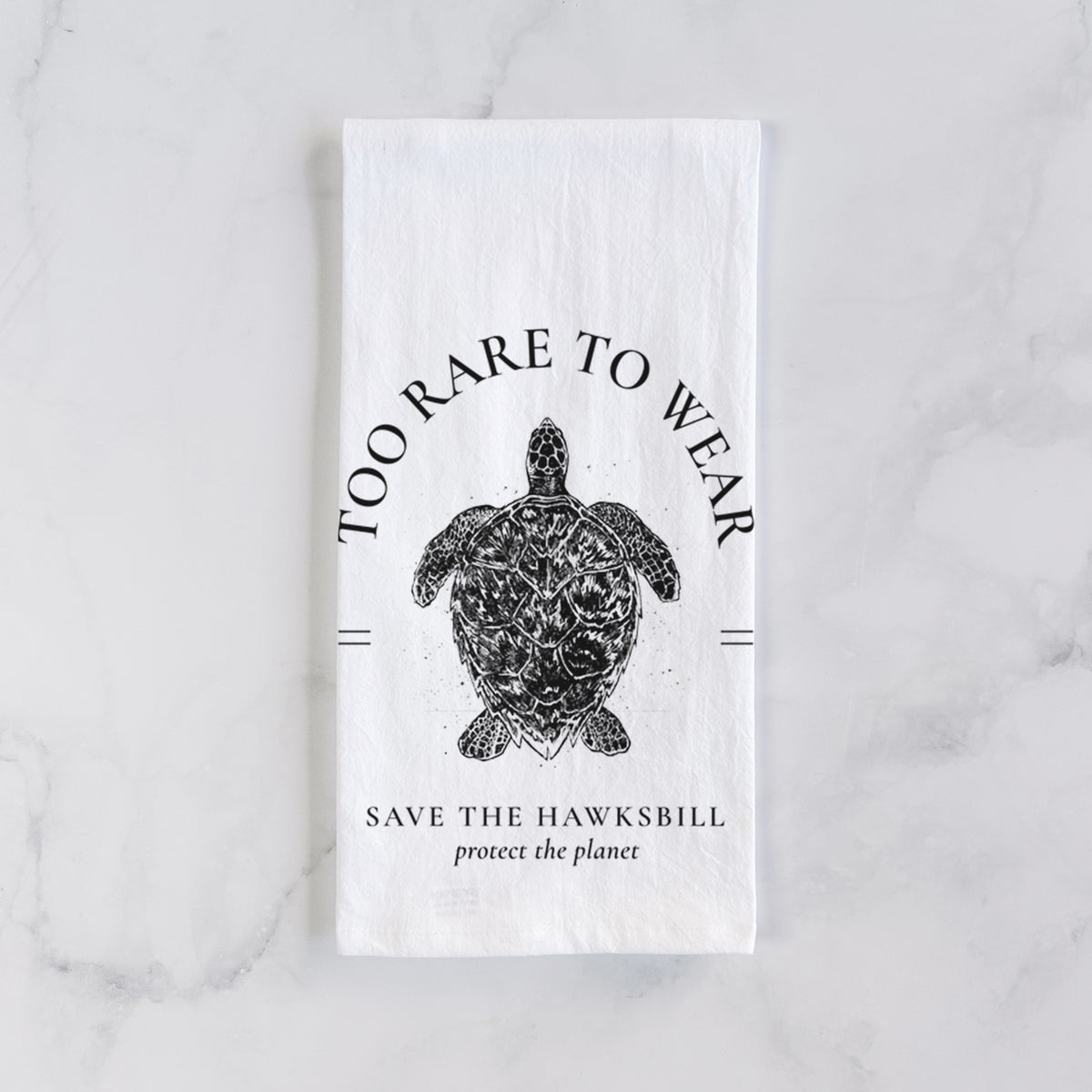White cotton tea towel laid flat on marble, printed with a black ink hawksbill sea turtle framed by the words Too Rare to Wear, Save the Hawksbill.