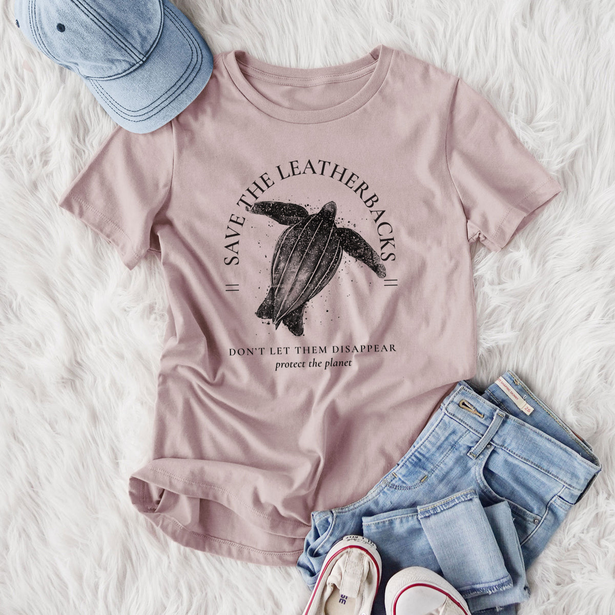Women's relaxed fit cotton t-shirt printed with a black ink leatherback sea turtle framed by the words Save the Leatherbacks, Don't Let Them Disappear, styled flat on a white faux fur rug with jeans.