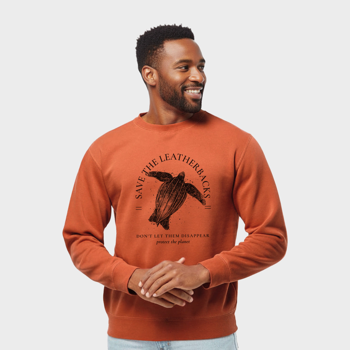 Model wearing an amber orange pigment dyed crewneck sweatshirt printed with a black ink leatherback sea turtle framed by the words Save the Leatherbacks, Don't Let Them Disappear.