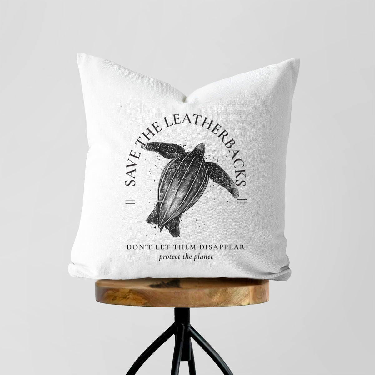 White pillow cover printed with a black ink leatherback sea turtle framed by the words Save the Leatherbacks, Don't Let Them Disappear, on a wooden stool.