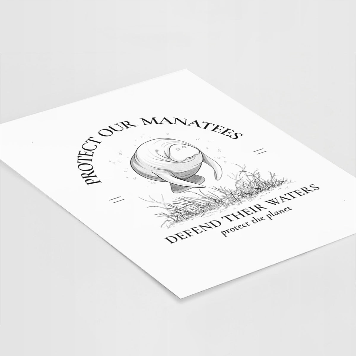 Art print of a black ink illustration of a manatee among seagrass, framed by the words Protect Our Manatees, Defend Their Waters, Protect the Planet, lying at an angle on a white surface.