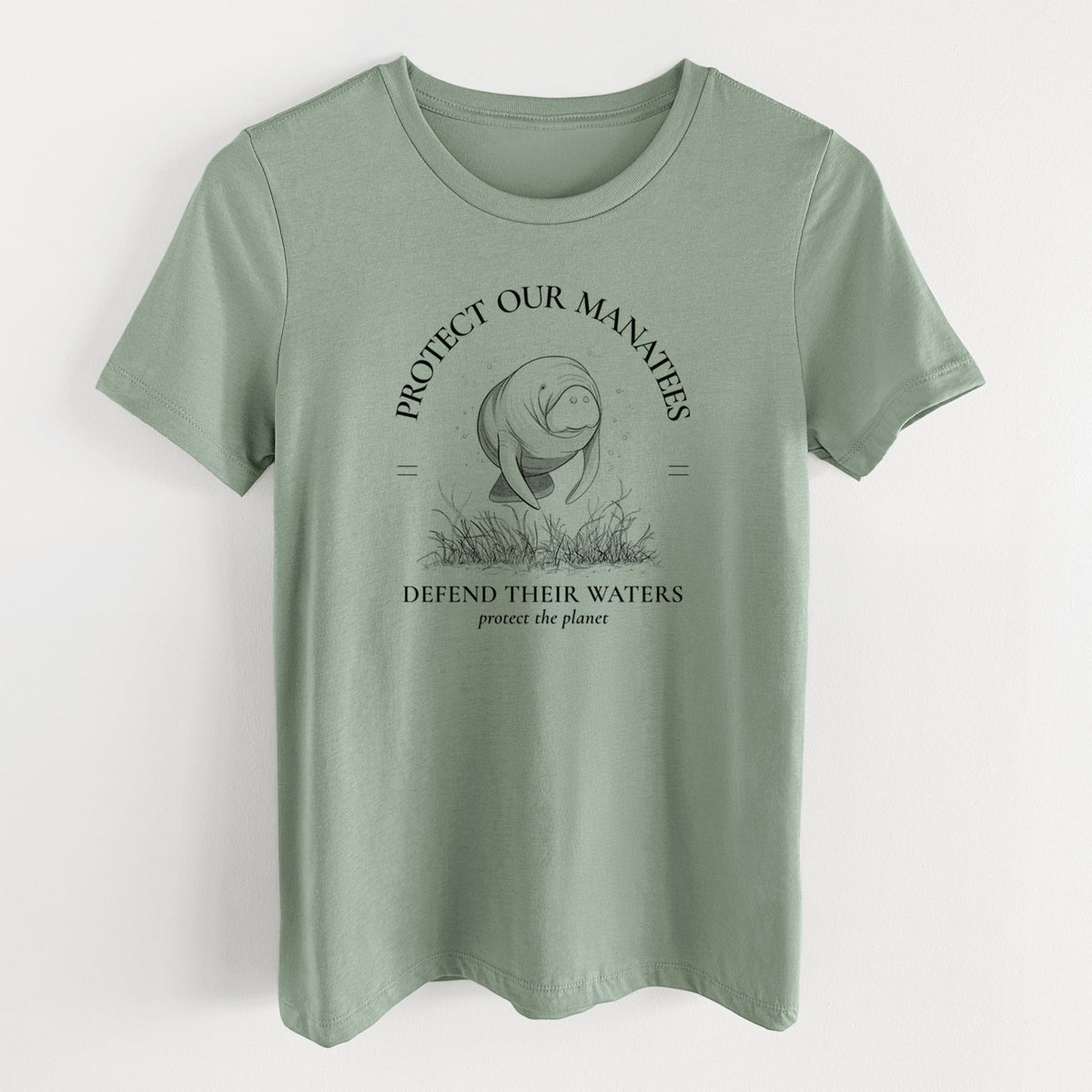 Sage green women's relaxed fit cotton t-shirt laid flat, printed with a black ink illustration of a manatee among seagrass, framed by the words Protect Our Manatees, Defend Their Waters, Protect the Planet.