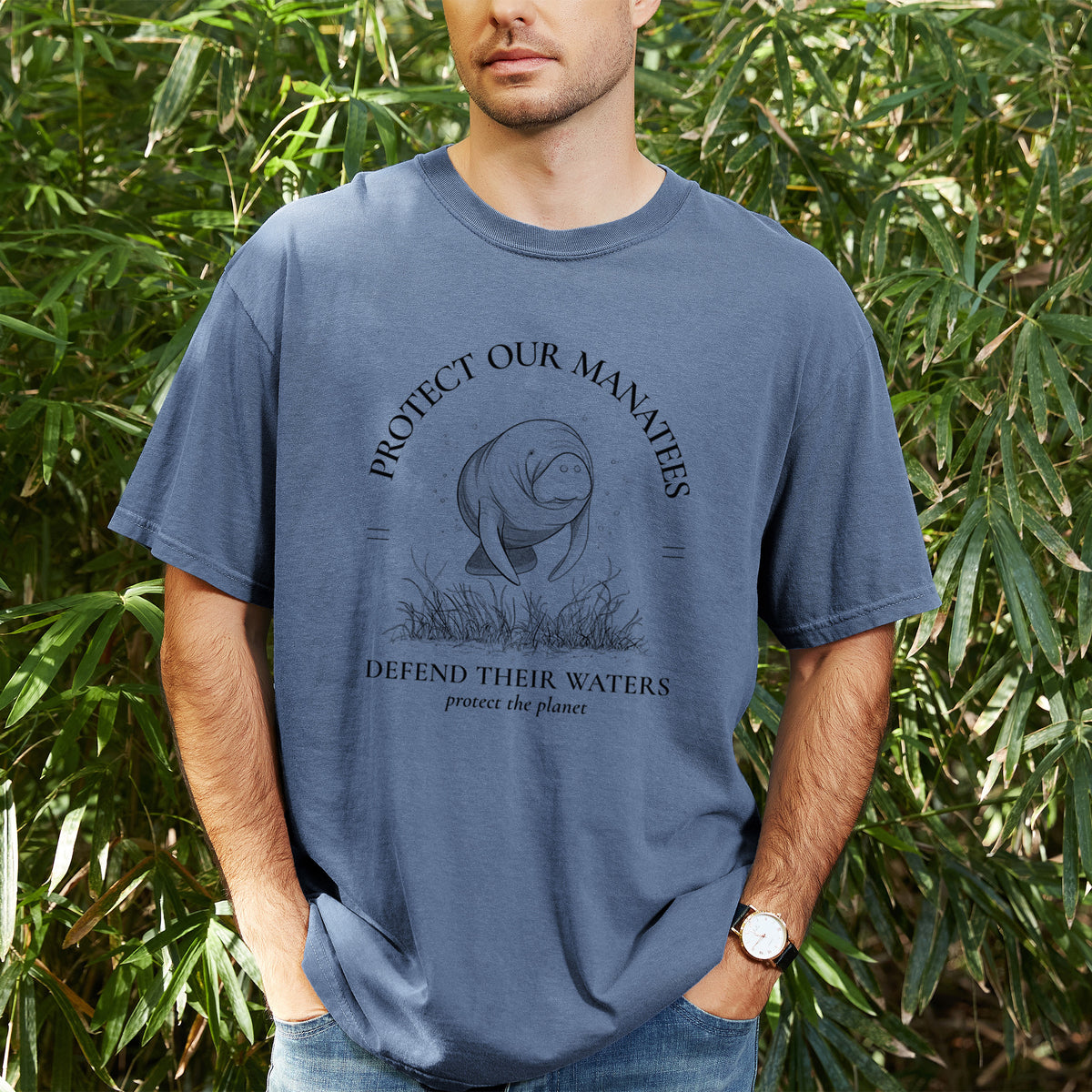 Man wearing a Comfort Colors t-shirt printed with a black ink illustration of a manatee among seagrass, framed by the words Protect Our Manatees, Defend Their Waters, Protect the Planet, outdoors.
