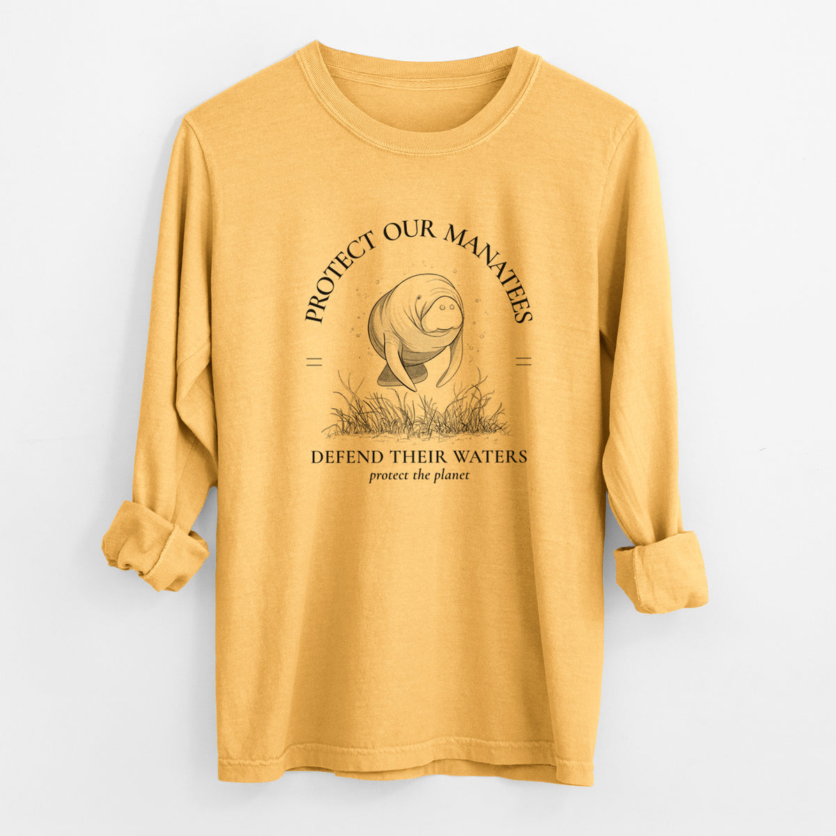 Golden wheat yellow Comfort Colors long sleeve shirt laid flat with the cuffs rolled, printed with a black ink illustration of a manatee among seagrass, framed by the words Protect Our Manatees, Defend Their Waters, Protect the Planet.