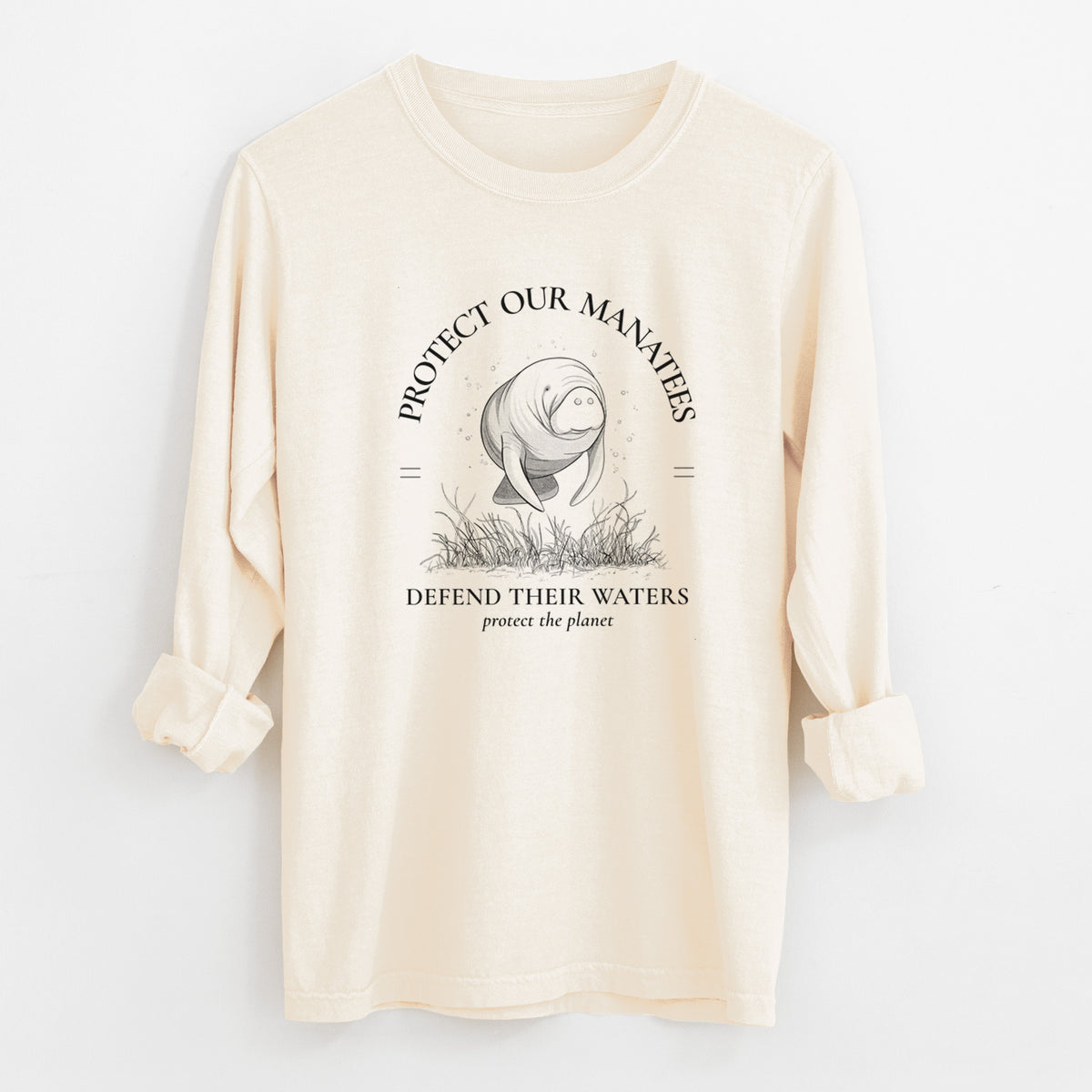 Ivory Comfort Colors long sleeve shirt laid flat with the cuffs rolled, printed with a black ink illustration of a manatee among seagrass, framed by the words Protect Our Manatees, Defend Their Waters, Protect the Planet.