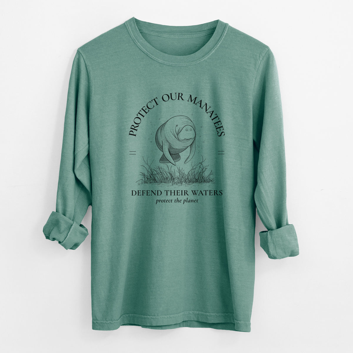 Pine green Comfort Colors long sleeve shirt laid flat with the cuffs rolled, printed with a black ink illustration of a manatee among seagrass, framed by the words Protect Our Manatees, Defend Their Waters, Protect the Planet.