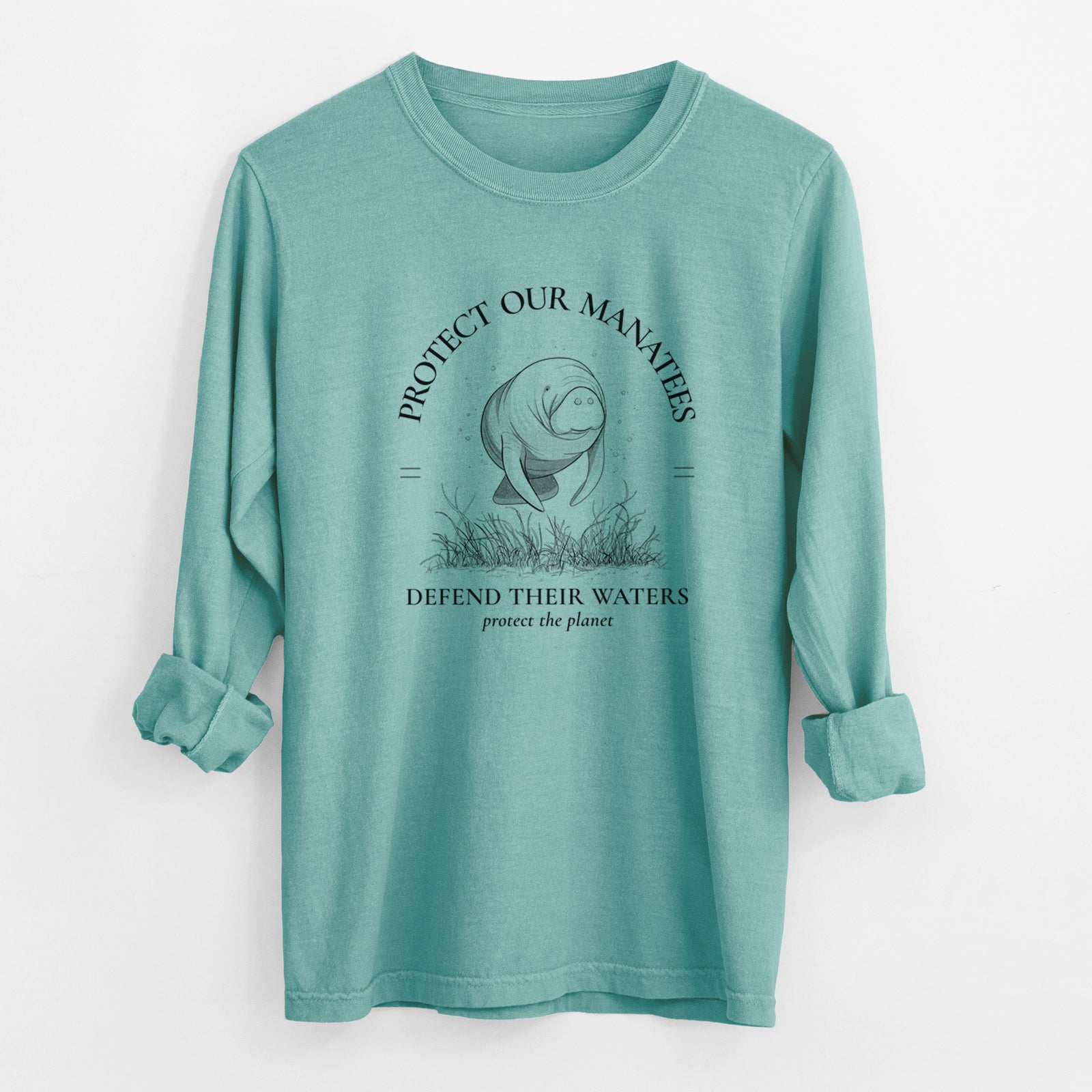 Reef green Comfort Colors long sleeve shirt laid flat with the cuffs rolled, printed with a black ink illustration of a manatee among seagrass, framed by the words Protect Our Manatees, Defend Their Waters, Protect the Planet.