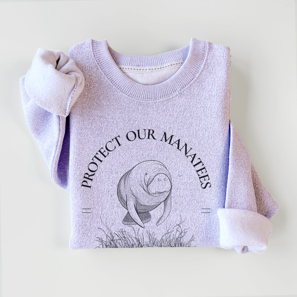 Ice purple knit sweatshirt printed with a black ink illustration of a manatee among seagrass, framed by the words Protect Our Manatees, Defend Their Waters, Protect the Planet, styled flat.