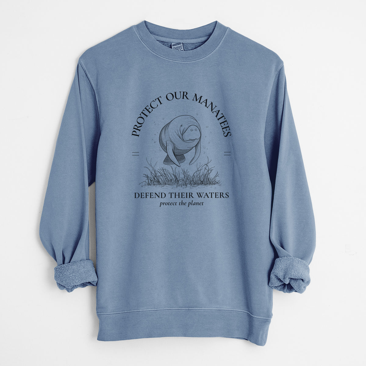 Slate blue pigment dyed crewneck sweatshirt laid flat with the sleeves rolled, printed with a black ink illustration of a manatee among seagrass, framed by the words Protect Our Manatees, Defend Their Waters, Protect the Planet.