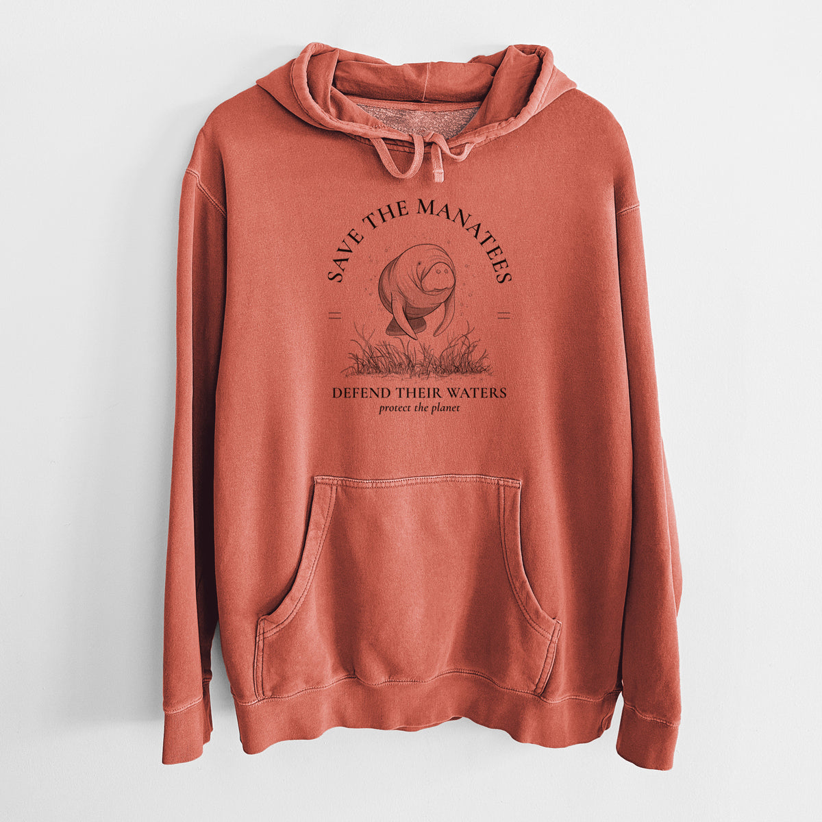 Amber orange pigment dyed hoodie laid flat, printed with a black ink illustration of a manatee among seagrass, framed by the words Protect Our Manatees, Defend Their Waters, Protect the Planet.