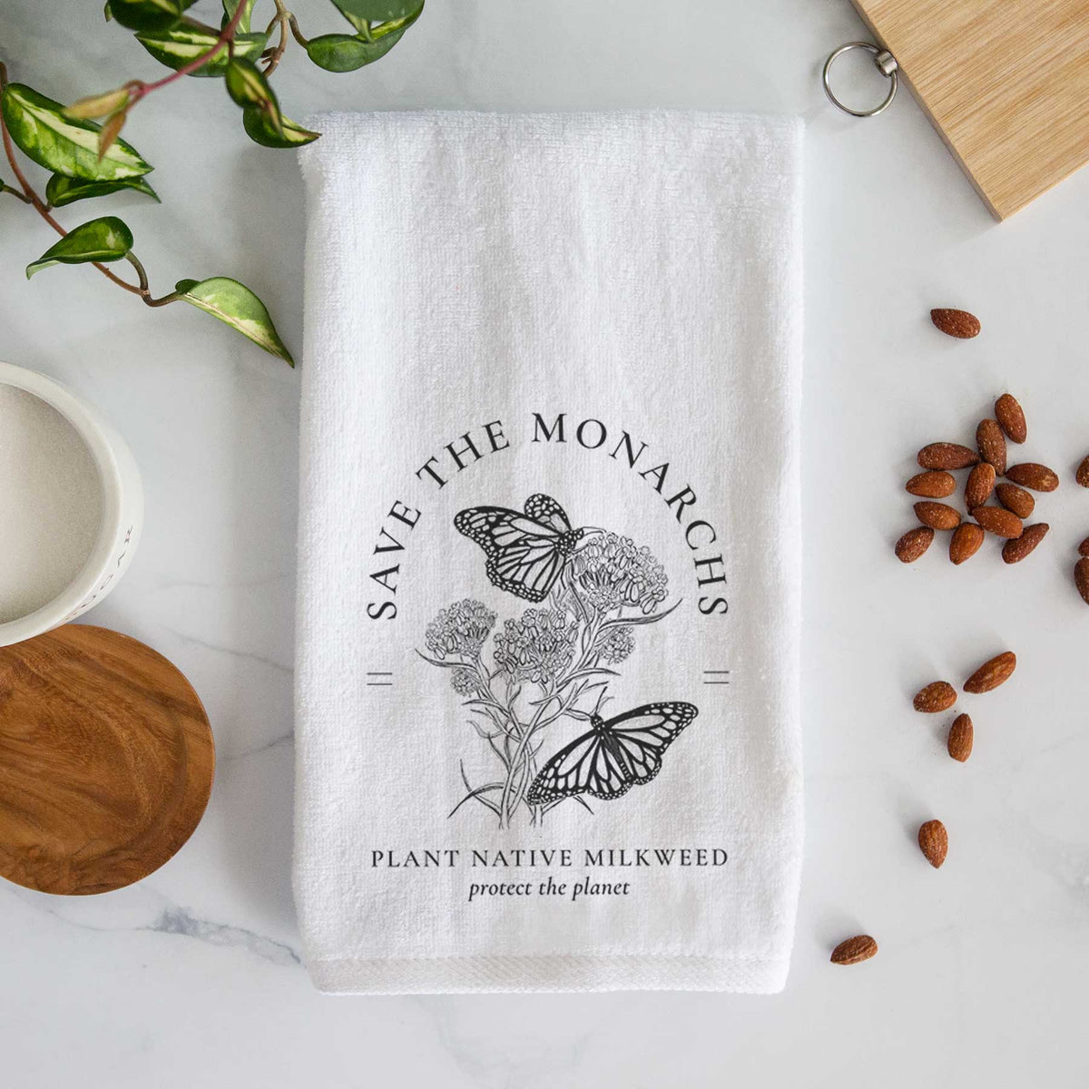 White hand towel printed with black ink monarch butterflies on milkweed flowers, framed by the words Save the Monarchs, Plant Native Milkweed.