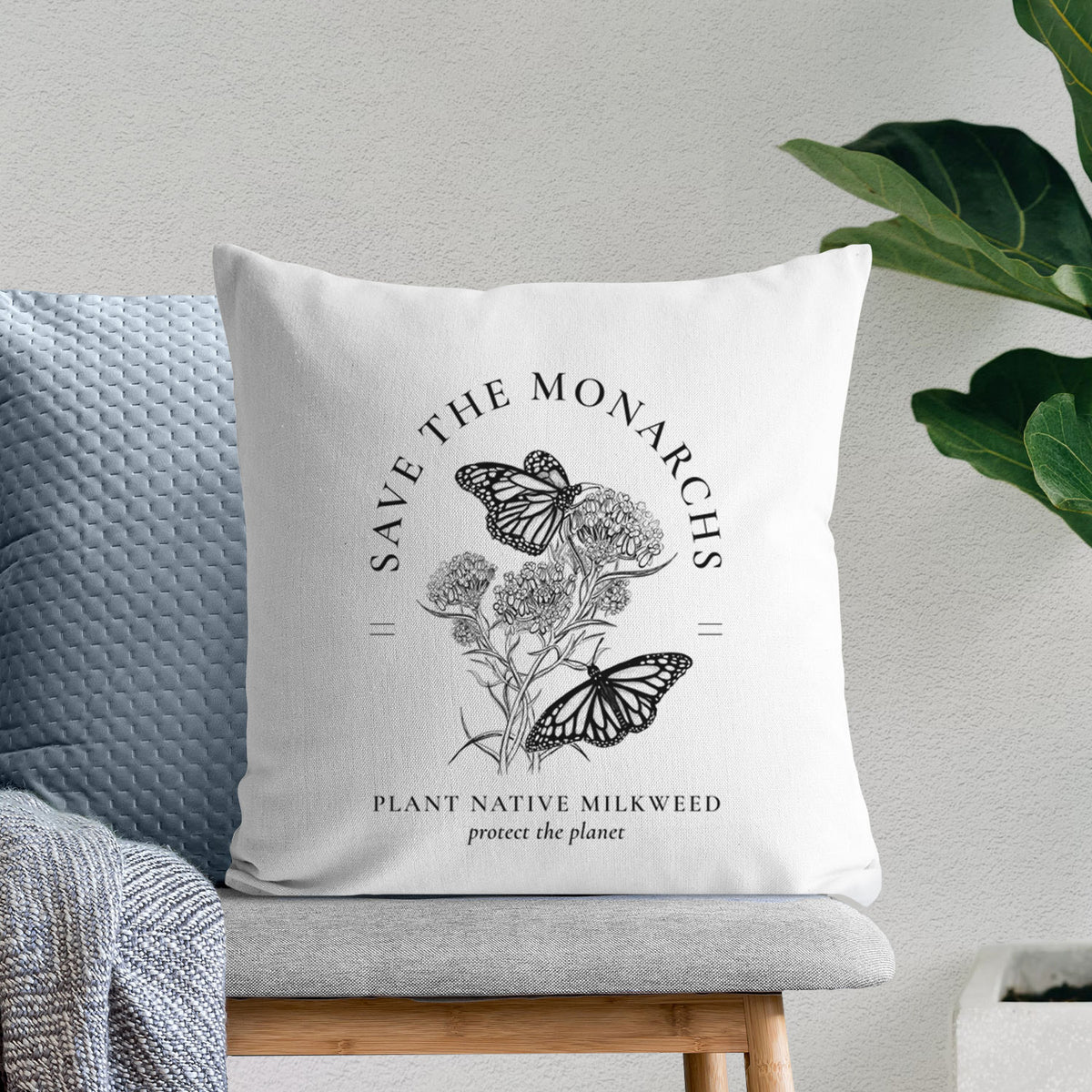 White pillow cover printed with black ink monarch butterflies on milkweed flowers, framed by the words Save the Monarchs, Plant Native Milkweed, on a bench beside plants.