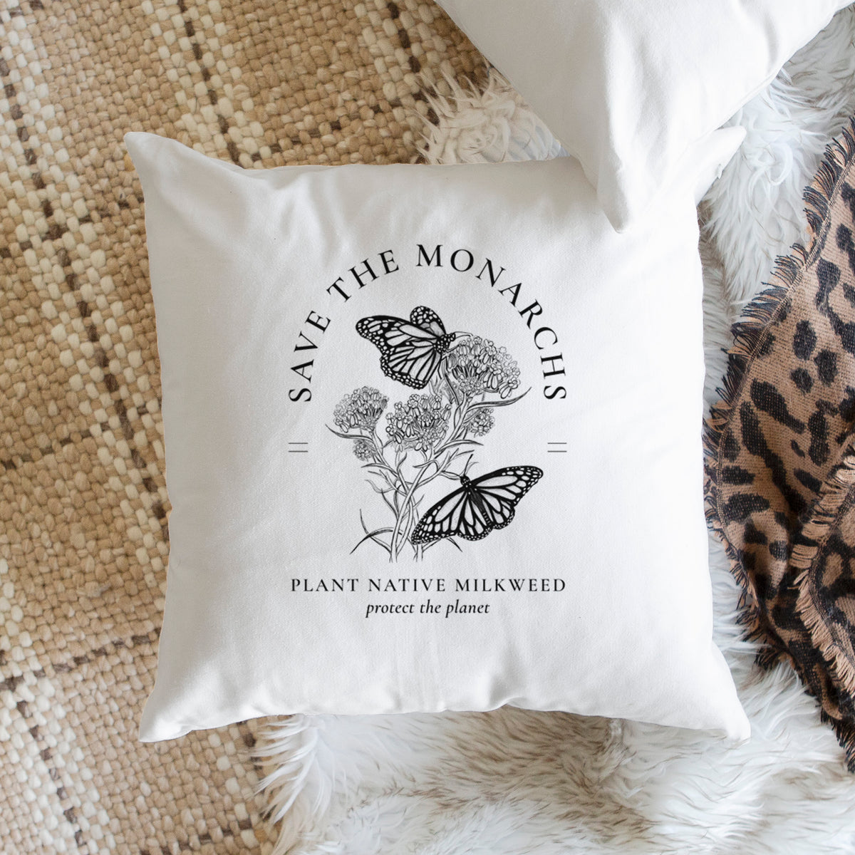 White pillow cover printed with black ink monarch butterflies on milkweed flowers, framed by the words Save the Monarchs, Plant Native Milkweed, on a woven chair.