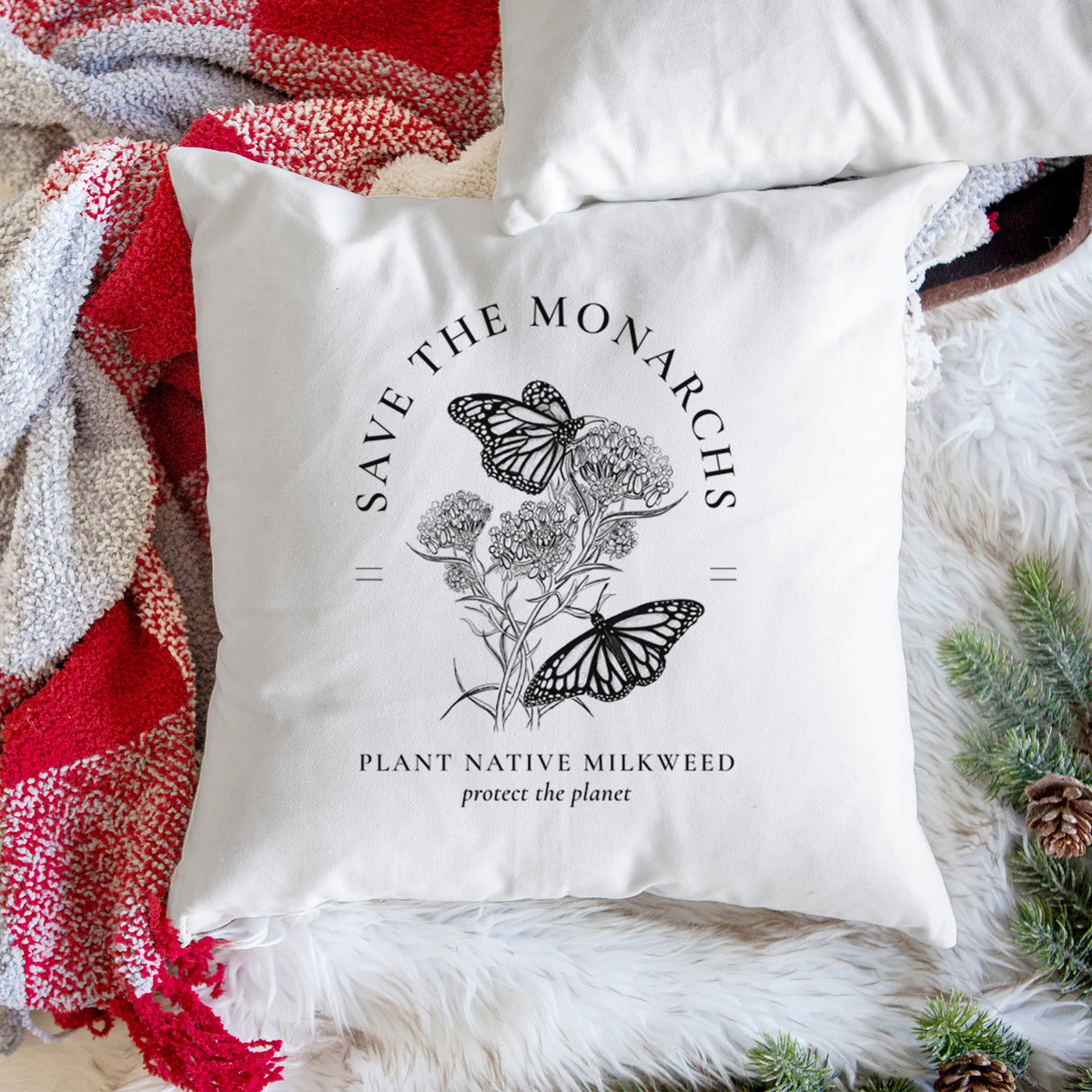 White pillow cover printed with black ink monarch butterflies on milkweed flowers, framed by the words Save the Monarchs, Plant Native Milkweed, on a woven chair.