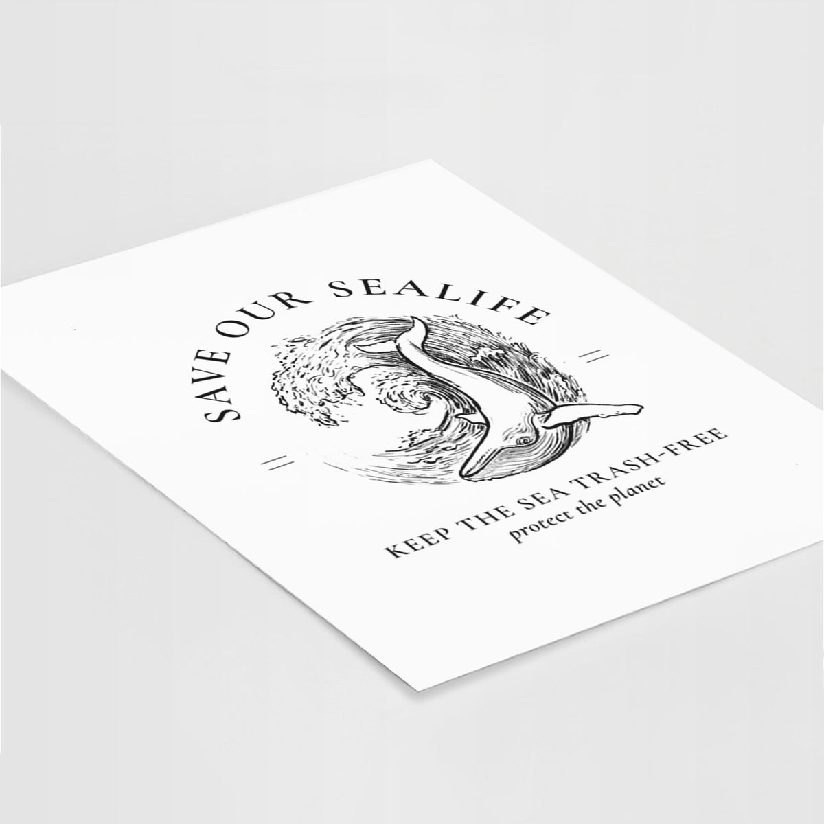 Art print of a black ink whale in an ocean wave framed by the words Save Our Sealife, Keep the Sea Trash-Free, lying at an angle on a white surface.