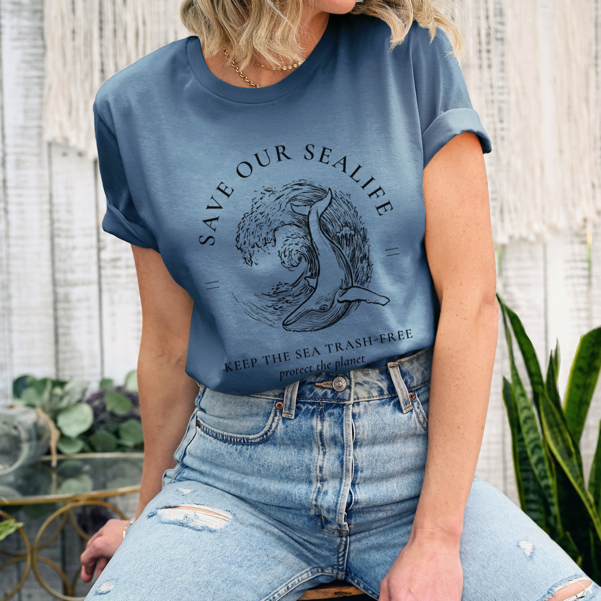 Woman wearing a steel blue lightweight cotton t-shirt printed with a black ink whale in an ocean wave framed by the words Save Our Sealife, Keep the Sea Trash-Free.