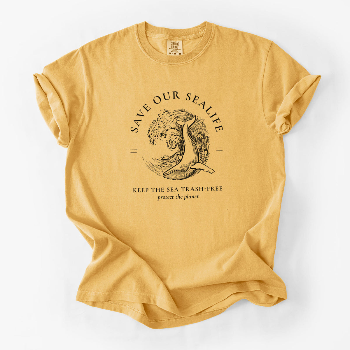 Golden wheat yellow Comfort Colors t-shirt laid flat, printed with a black ink whale in an ocean wave framed by the words Save Our Sealife, Keep the Sea Trash-Free.