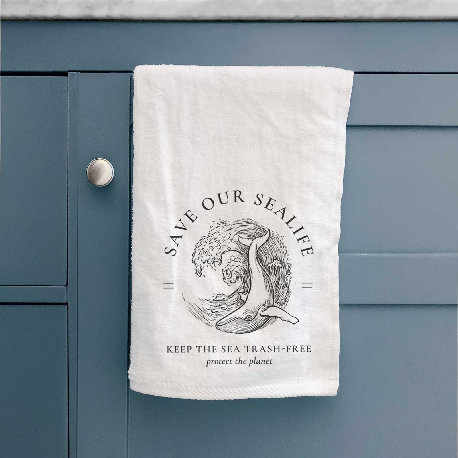 White hand towel printed with a black ink whale in an ocean wave framed by the words Save Our Sealife, Keep the Sea Trash-Free.