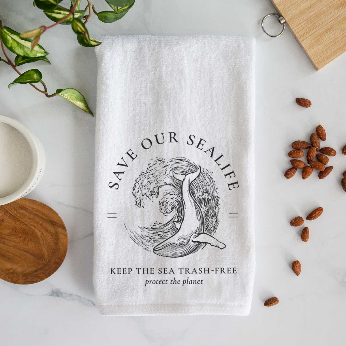White hand towel printed with a black ink whale in an ocean wave framed by the words Save Our Sealife, Keep the Sea Trash-Free.