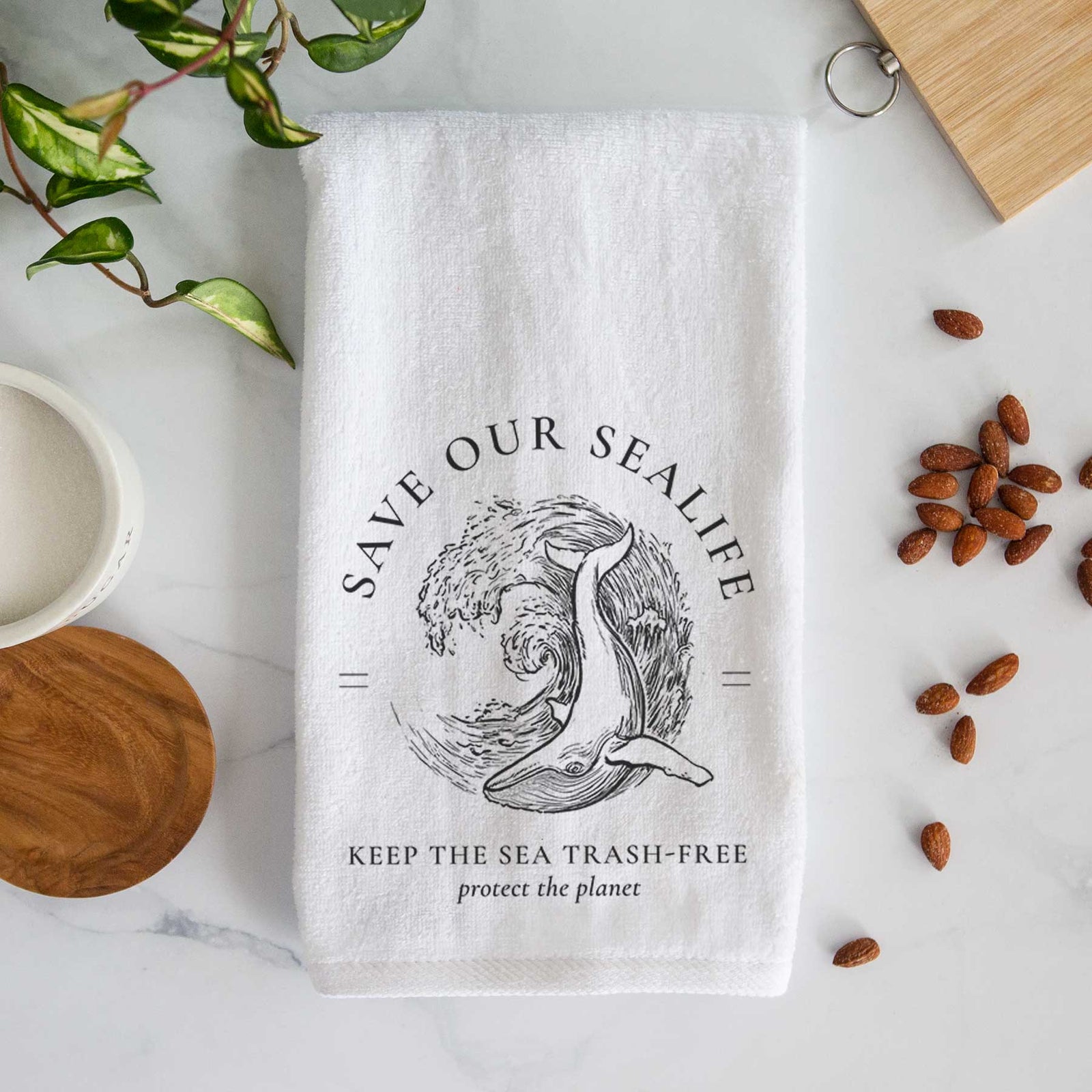 White hand towel printed with a black ink whale in an ocean wave framed by the words Save Our Sealife, Keep the Sea Trash-Free.