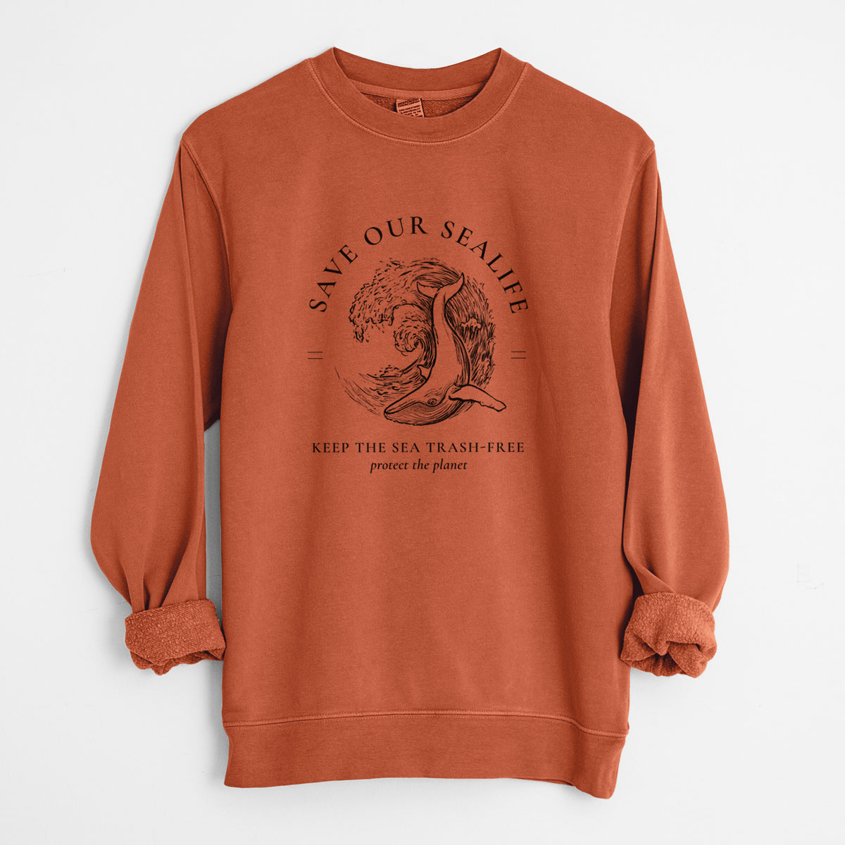 Amber orange pigment dyed crewneck sweatshirt laid flat with the sleeves rolled, printed with a black ink whale in an ocean wave framed by the words Save Our Sealife, Keep the Sea Trash-Free.
