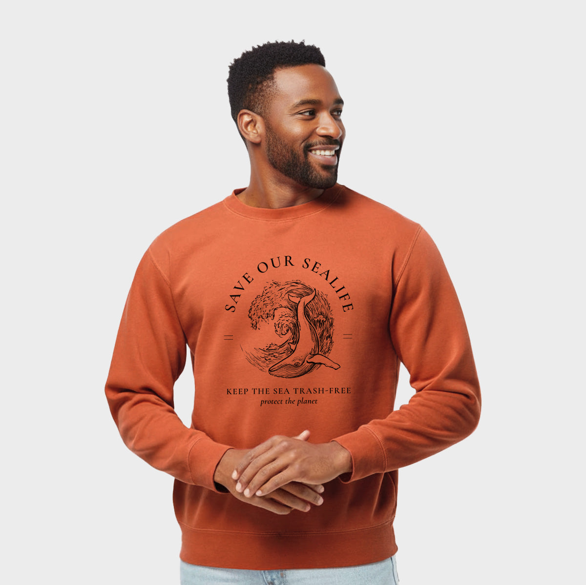 Model wearing an amber orange pigment dyed crewneck sweatshirt printed with a black ink whale in an ocean wave framed by the words Save Our Sealife, Keep the Sea Trash-Free.