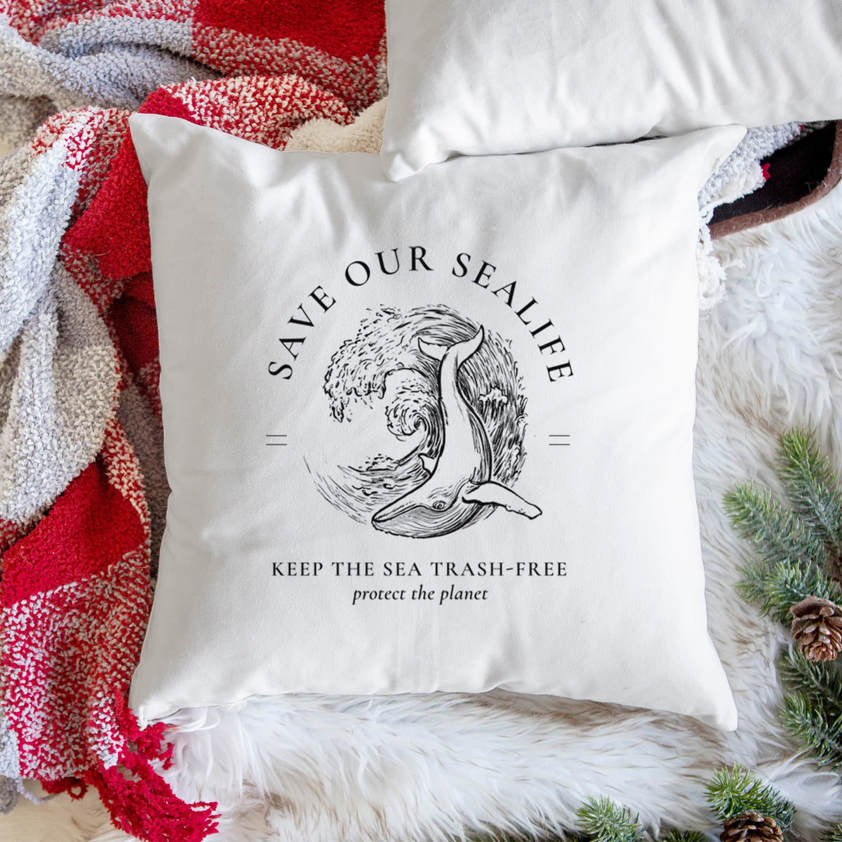White pillow cover printed with a black ink whale in an ocean wave framed by the words Save Our Sealife, Keep the Sea Trash-Free, on a woven chair.
