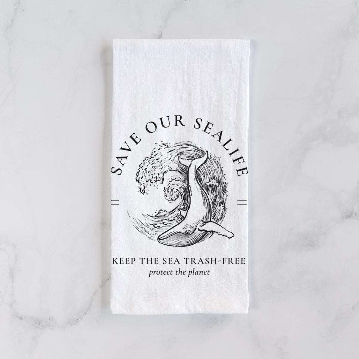 White cotton tea towel laid flat on marble, printed with a black ink whale in an ocean wave framed by the words Save Our Sealife, Keep the Sea Trash-Free.