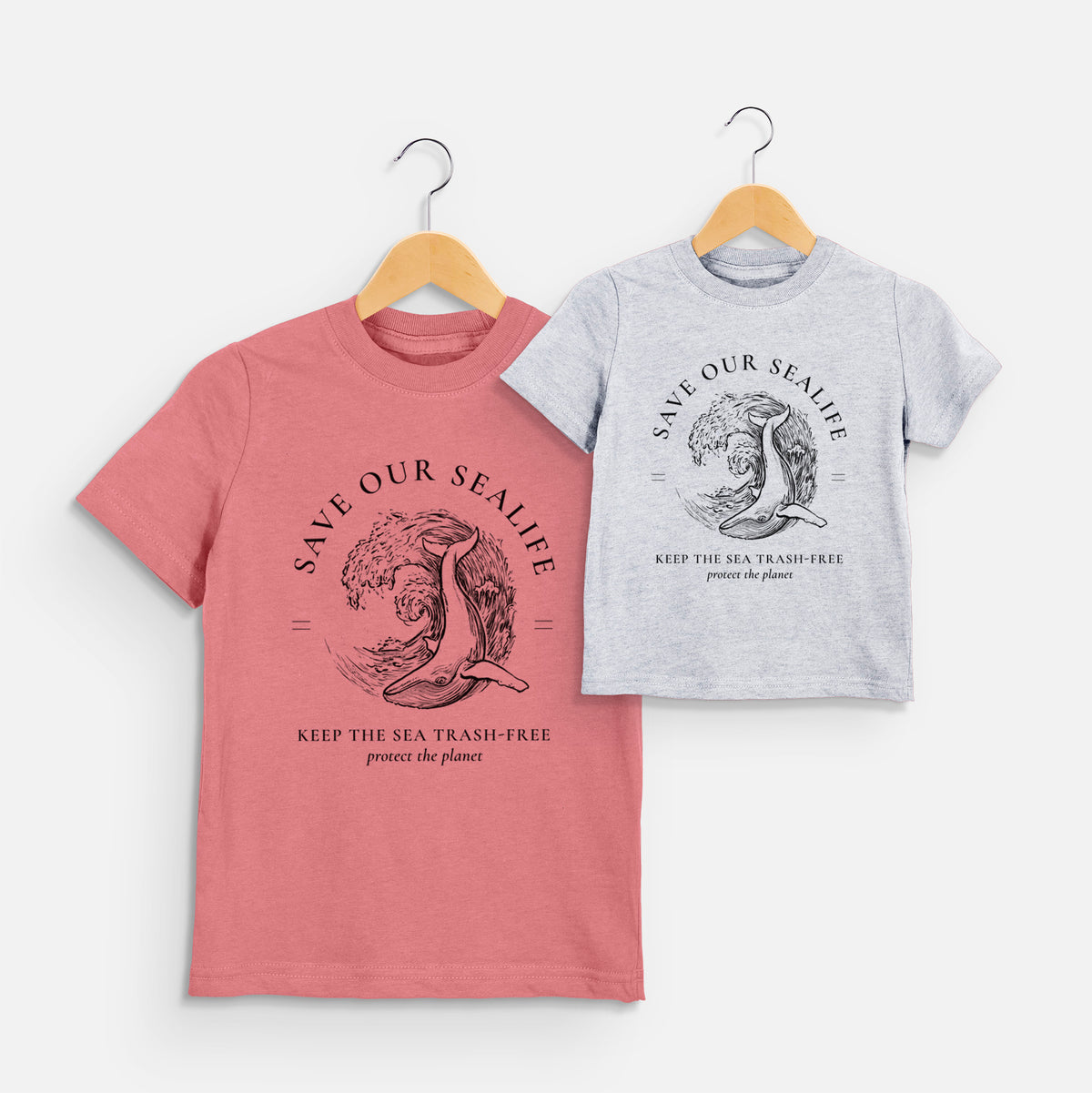 Two youth t-shirts in different colors on hangers, printed with a black ink whale in an ocean wave framed by the words Save Our Sealife, Keep the Sea Trash-Free.