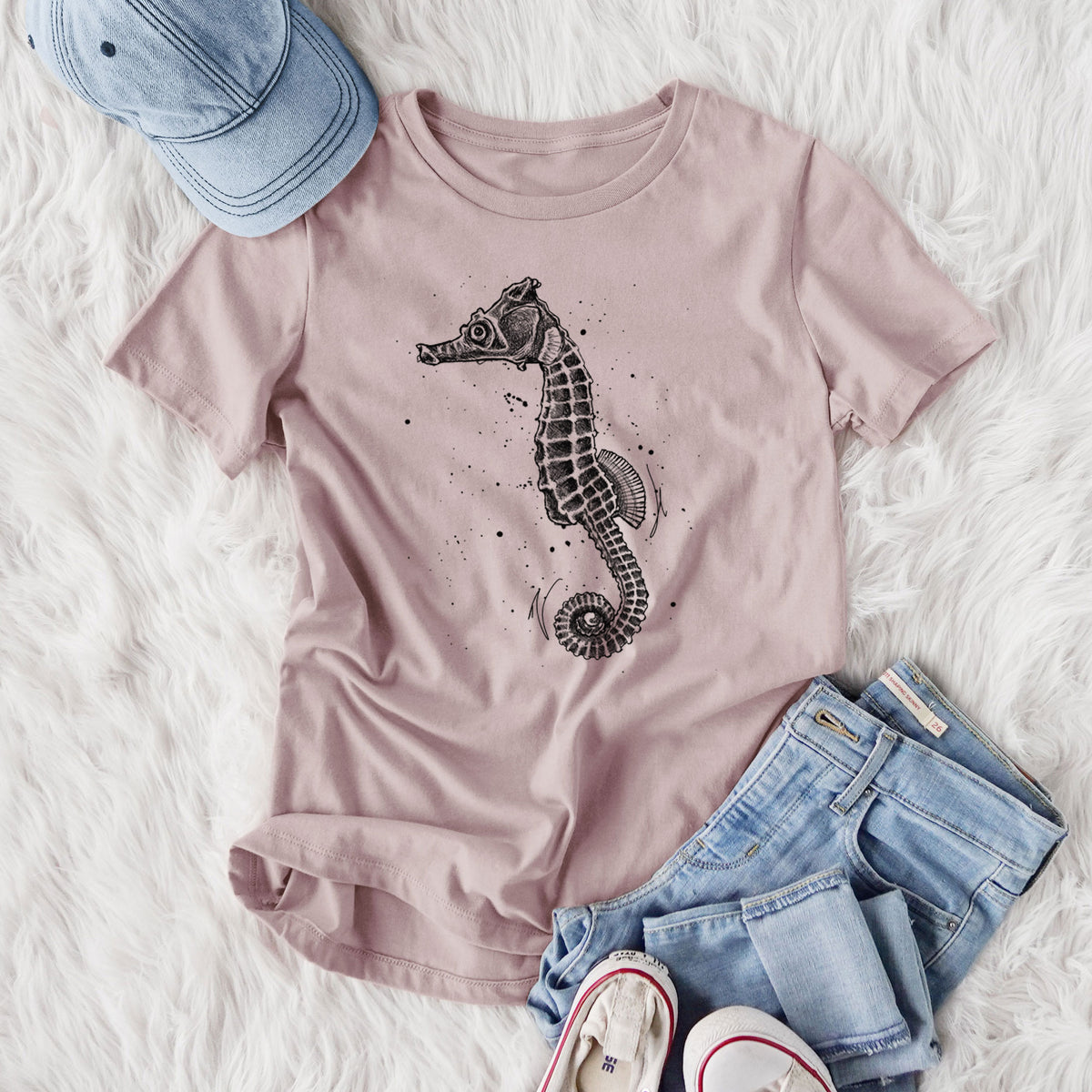 Women's relaxed fit cotton t-shirt printed with a detailed black ink illustration of a Pacific seahorse with its tail curled, styled flat on a white faux fur rug with jeans.