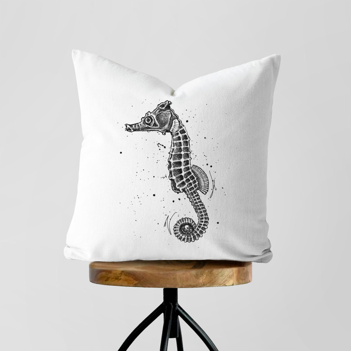 White pillow cover printed with a detailed black ink illustration of a Pacific seahorse with its tail curled, on a wooden stool.