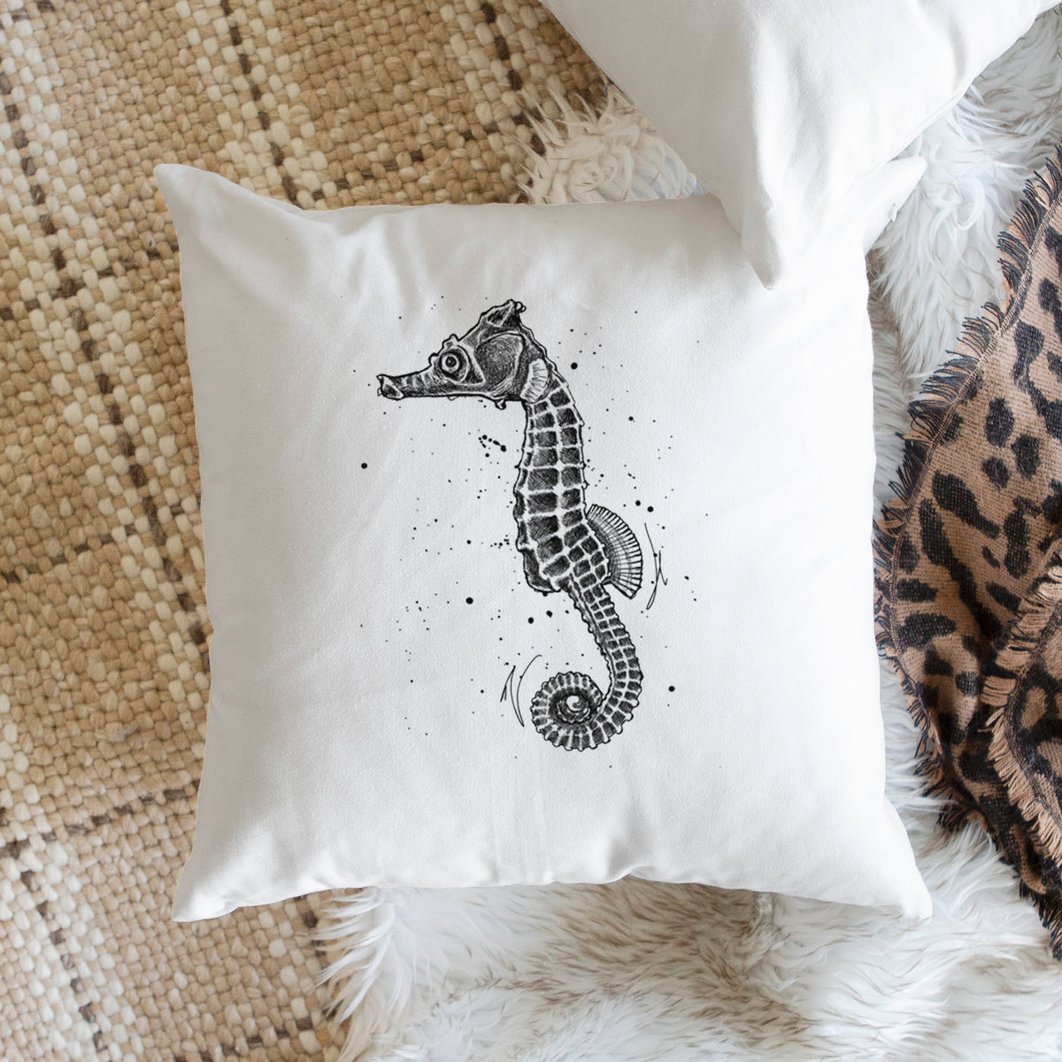 White pillow cover printed with a detailed black ink illustration of a Pacific seahorse with its tail curled, on a woven chair.