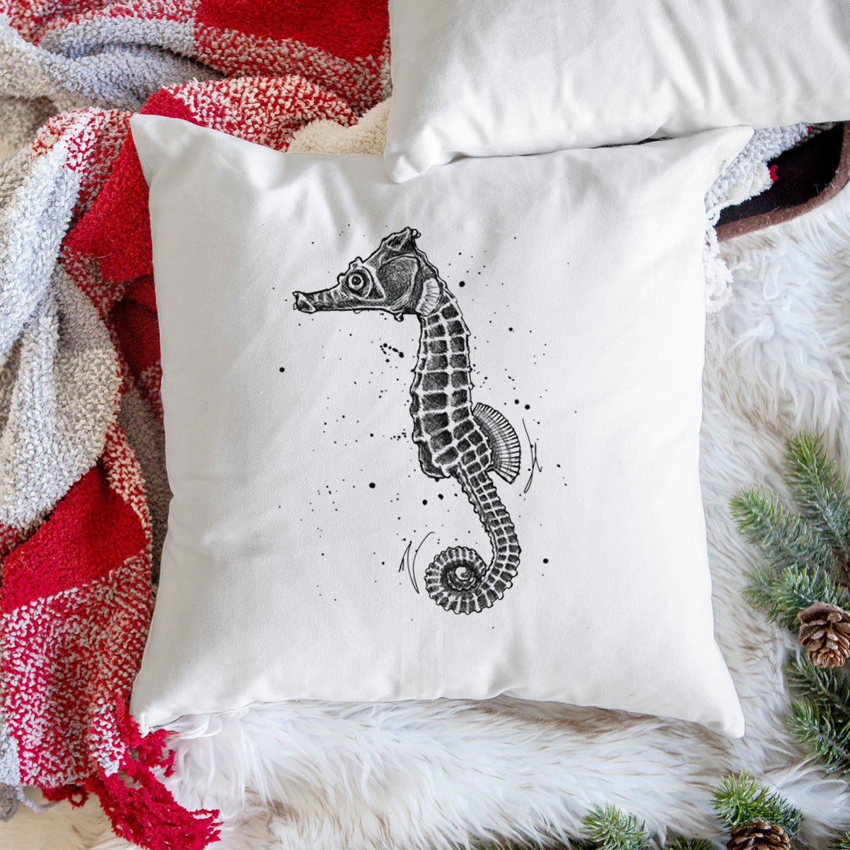 White pillow cover printed with a detailed black ink illustration of a Pacific seahorse with its tail curled, on a woven chair.