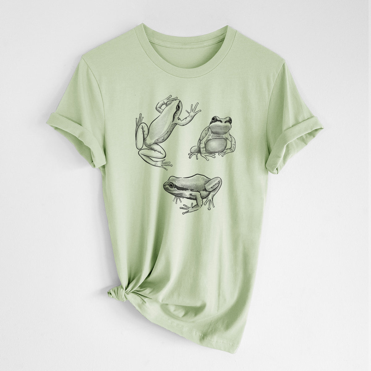Spring green lightweight cotton t-shirt laid flat with the sleeves rolled, printed with a black ink illustration of three Pacific tree frogs in different poses.