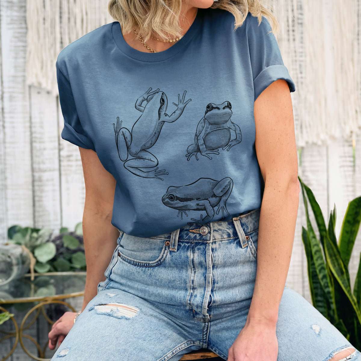 Woman wearing a steel blue lightweight cotton t-shirt printed with a black ink illustration of three Pacific tree frogs in different poses.
