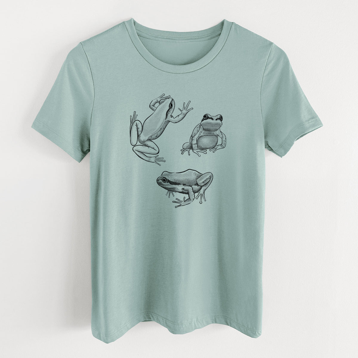 Dusty blue women's relaxed fit cotton t-shirt laid flat, printed with a black ink illustration of three Pacific tree frogs in different poses.