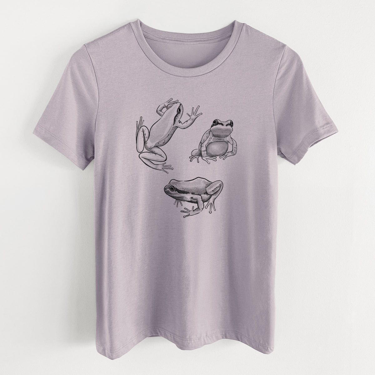 Light violet women's relaxed fit cotton t-shirt laid flat, printed with a black ink illustration of three Pacific tree frogs in different poses.