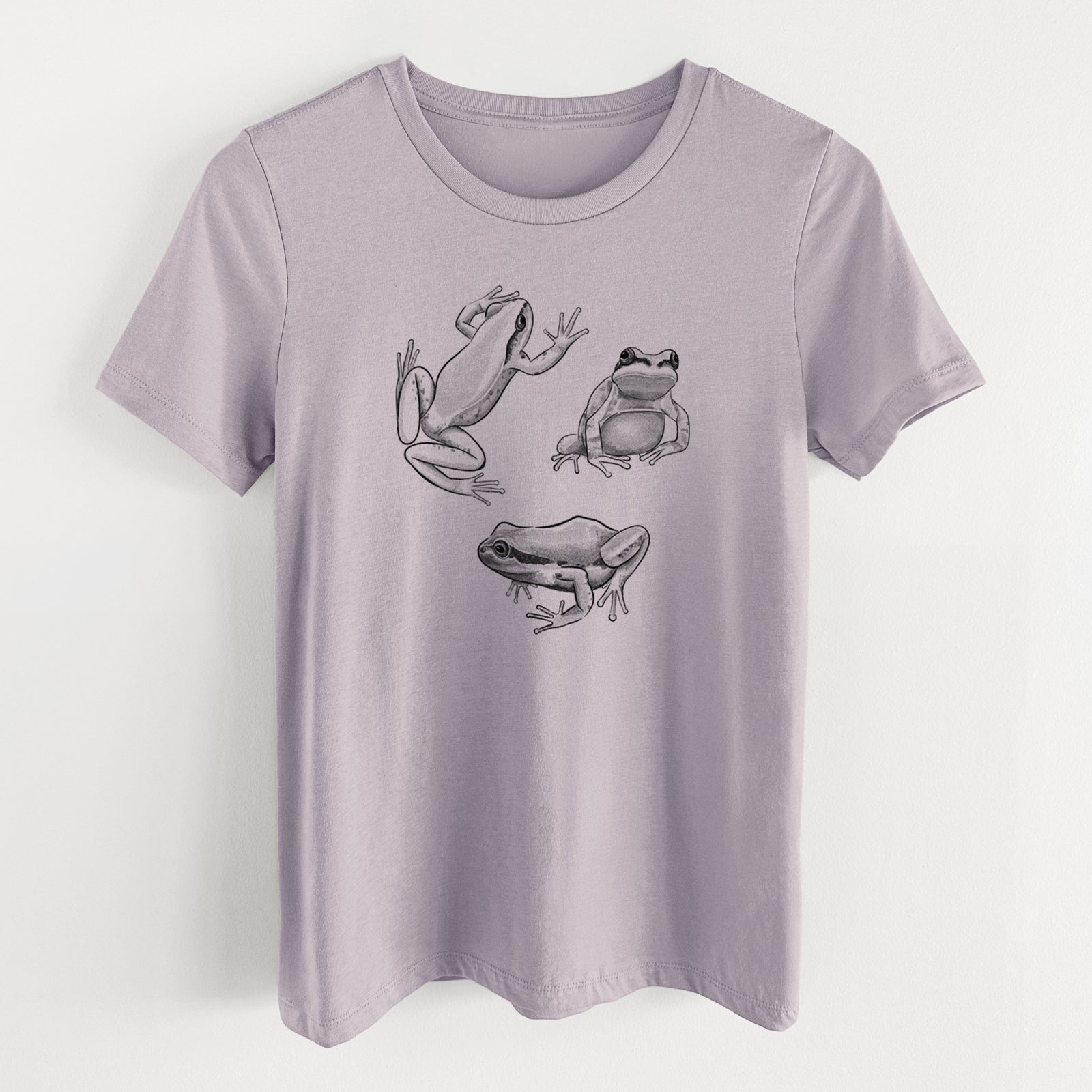 Light violet women's relaxed fit cotton t-shirt laid flat, printed with a black ink illustration of three Pacific tree frogs in different poses.