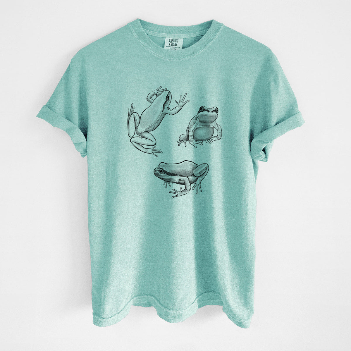 Chalky mint Comfort Colors t-shirt laid flat, printed with a black ink illustration of three Pacific tree frogs in different poses.