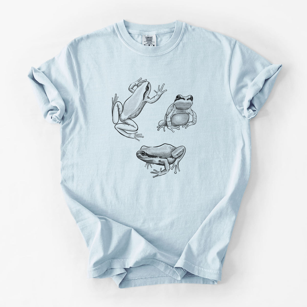 Chambray blue Comfort Colors t-shirt laid flat, printed with a black ink illustration of three Pacific tree frogs in different poses.